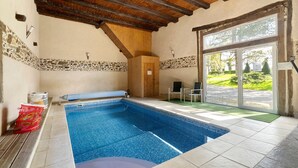 Una piscina con borde de piedra, vigas de techo de madera y vistas al exterior.