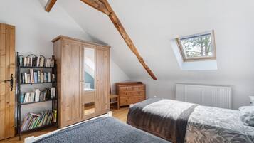 Een slaapkamer met een schuine kap, een houten garderobe, een boekenkast, een raam en een radiator.