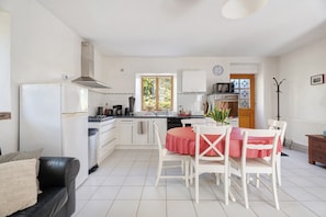 A kitchen with white cabinets, a dining table with a red tablecloth, and a black leather sofa.