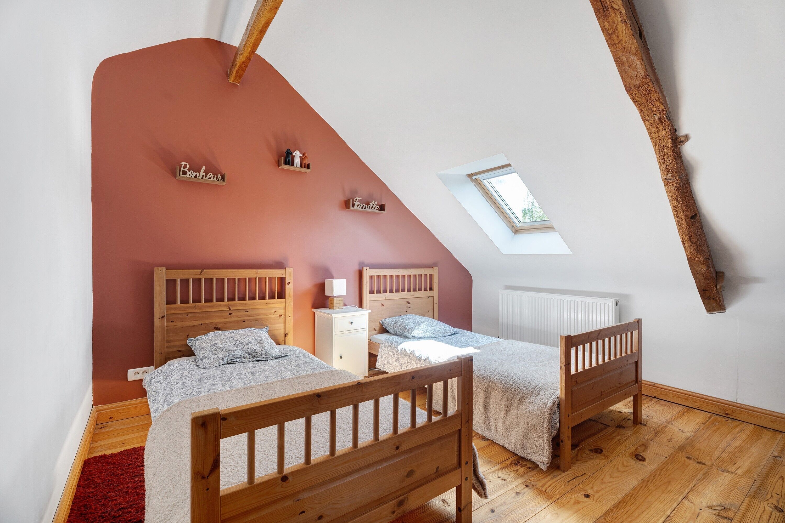 A bedroom with two wooden beds, a red accent wall, a skylight, and a small window.