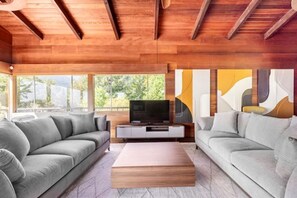 A modern living room with a wooden ceiling, two grey sofas, a wooden coffee table, and a TV on a white stand.