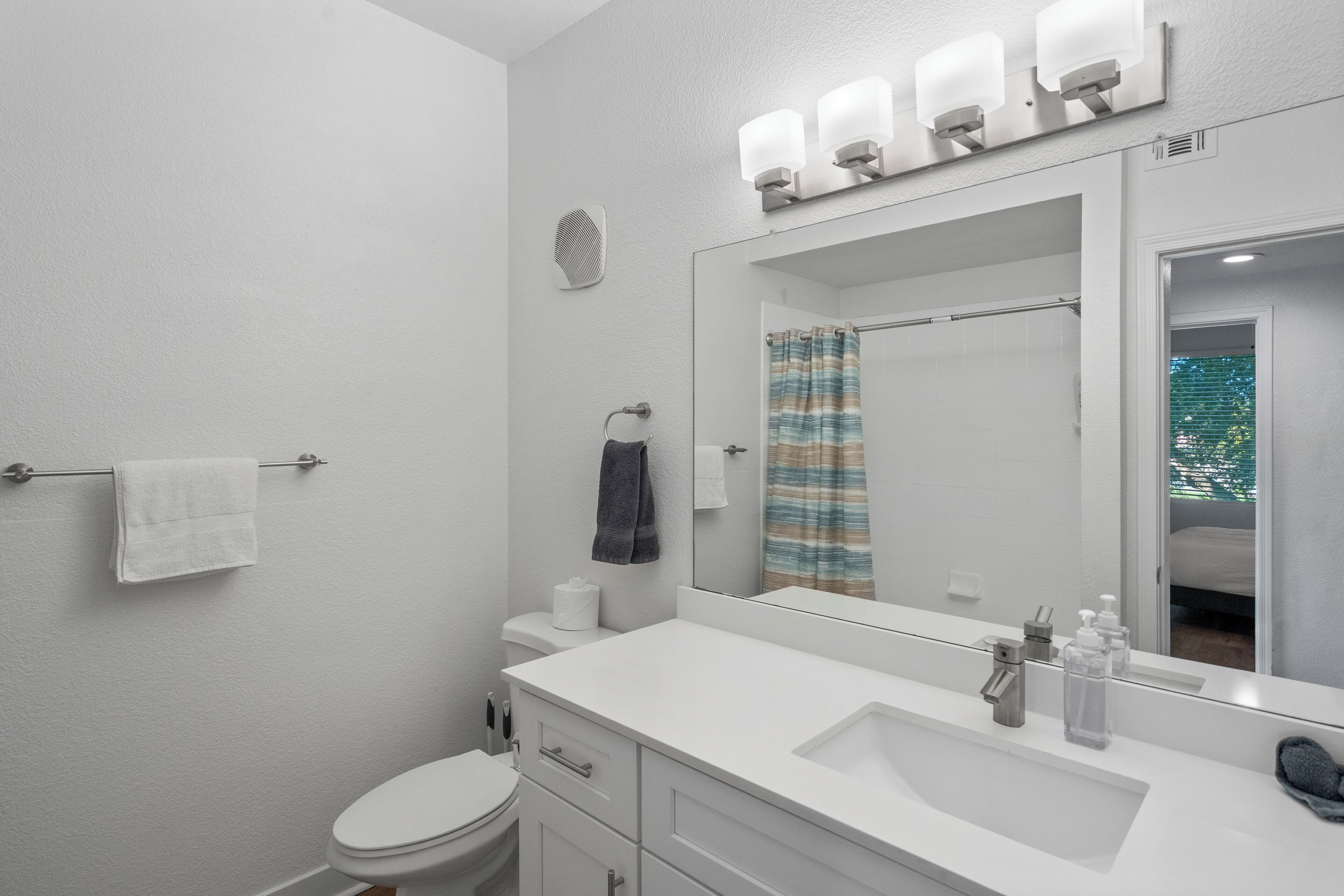 A bathroom with a white sink, mirror, towel rack, and a shower curtain.