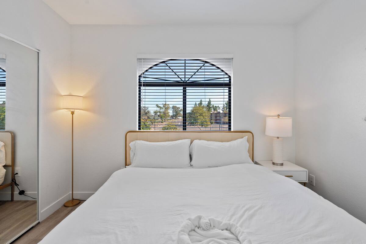 Une chambre d’hôtel avec un lit, une table de chevet, une lampe, une fenêtre donnant sur un beau paysage et un miroir.