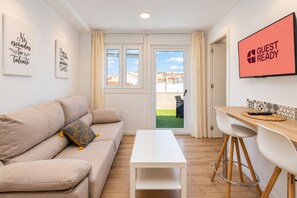 Una sala de estar moderna con un sofá, una mesa de comedor y una pantalla de televisión mostrando 'GUEST READY'.