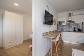 Uma cozinha moderna com uma mesa de jantar de madeira, cadeiras brancas, uma TV e um micro-ondas.