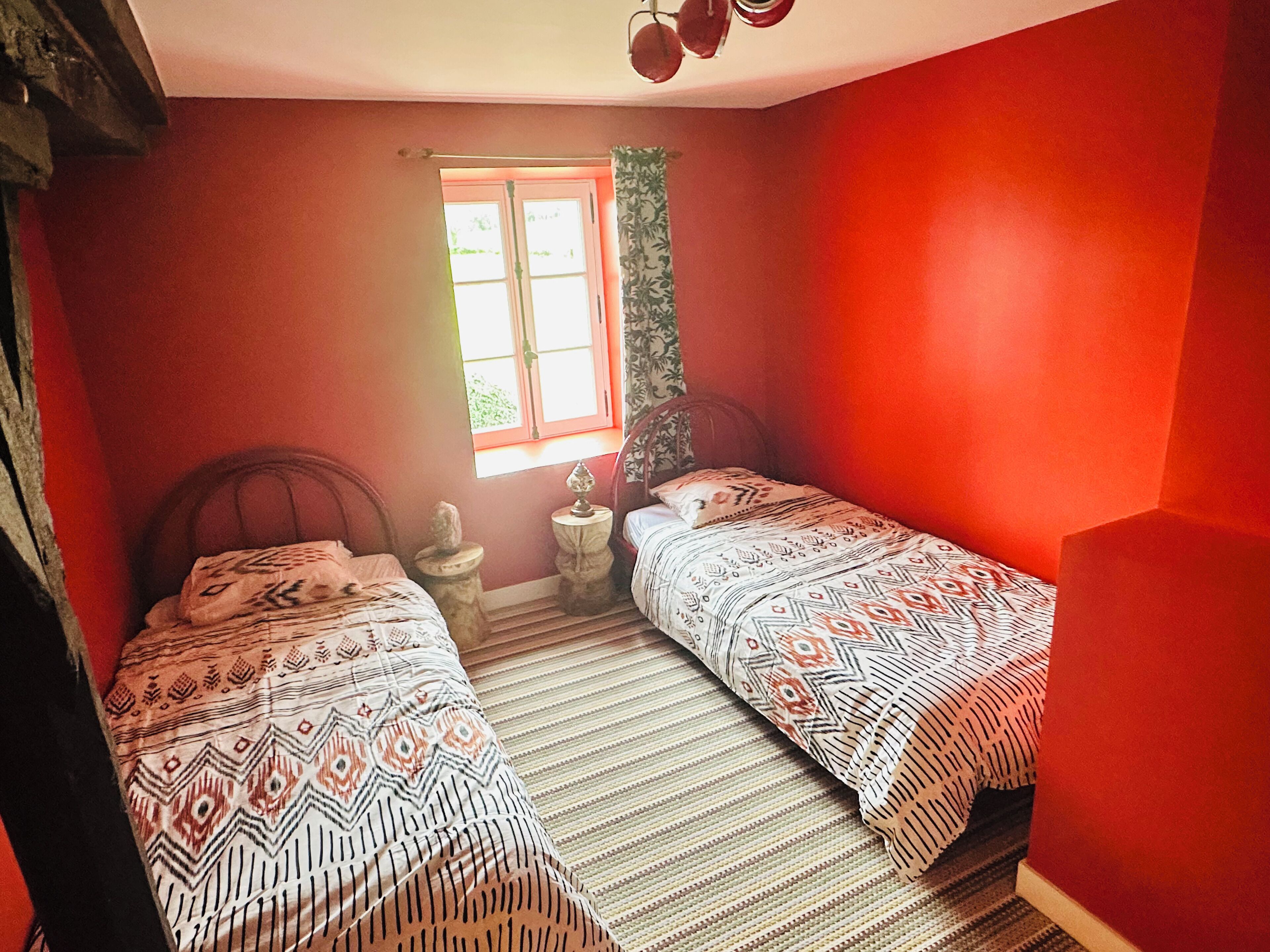A room with two beds, a window with curtains, and a small table with a lamp.