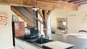 A kitchen with a central island, wooden beams, and pendant lighting. - Gîte du Alchimiste on the Château de Dompierre estate (Dompierre-les-Églises)