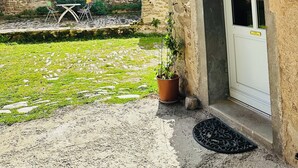 A rustic outdoor area with a stone wall, a wooden pergola with hanging cloth, a potted plant, and a door with a sign. - Gîte du Alchimiste on the Château de Dompierre estate (Dompierre-les-Églises)