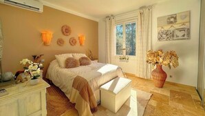 Quarto com cama, mesas de cabeceira, cômoda, janela com cortinas e decoração nas paredes.