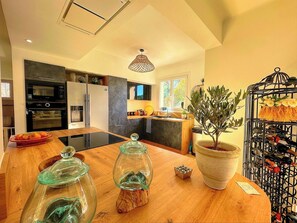 Une cuisine moderne avec un îlot central en bois, des appareils électroménagers intégrés et un arbre en pot.
