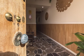 A wooden door with brass handles and a keyhole, a stone-tiled floor, and a wooden wall with a circular design. - GuestReady - Palacio San Juan Attic 13 (El Puerto de Santa María)