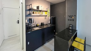 A modern kitchen with a black countertop, a coffee machine, and a shelf with kitchen items. - Rio Select - Copacabana  (Rio de Janeiro)