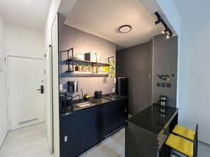 A modern kitchen with a black countertop, a coffee machine, and a shelf with kitchen items. - Rio Select - Copacabana  (Rio de Janeiro)