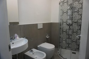 A bathroom with a sink, bidet, toilet, and a shower with patterned tiles. - Holiday Rooms (Florence)