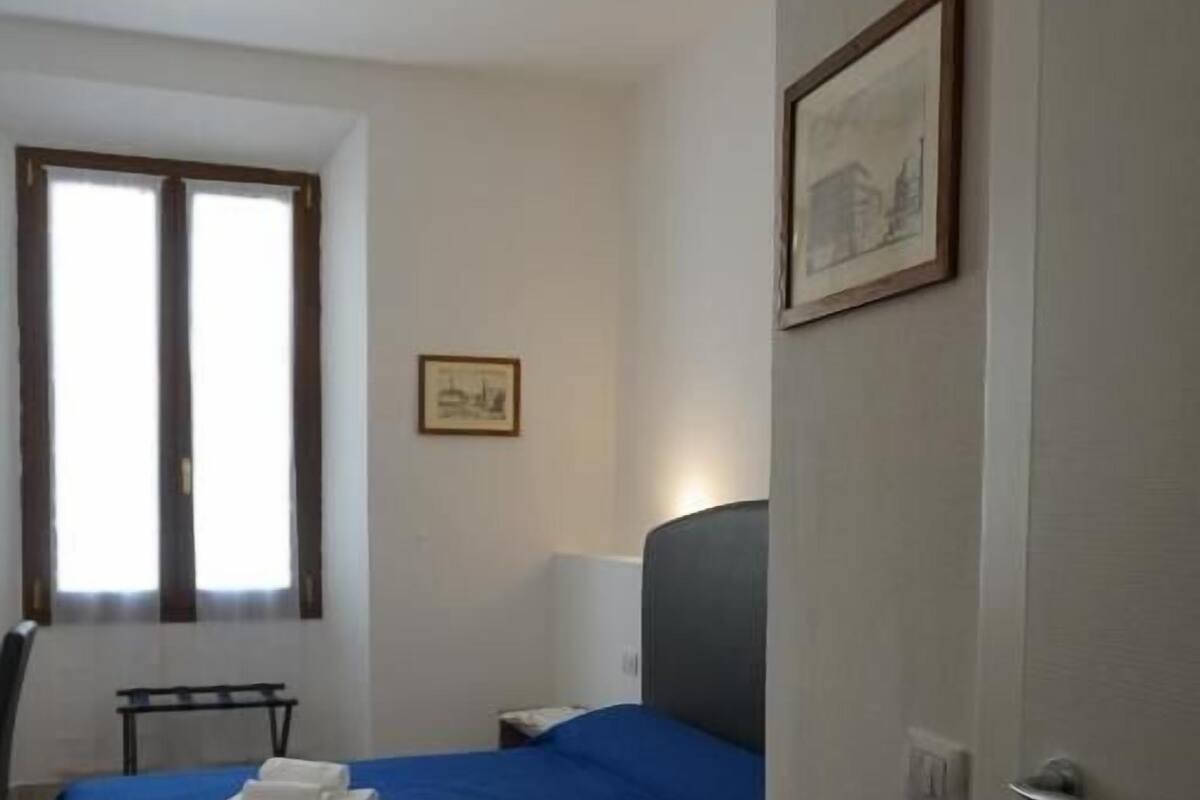 A room with a bed, a chair, a desk, a window, and a door.