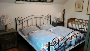 A bedroom with a bed, two bedside tables, a nightstand, a crib, and a wall-mounted shelf.