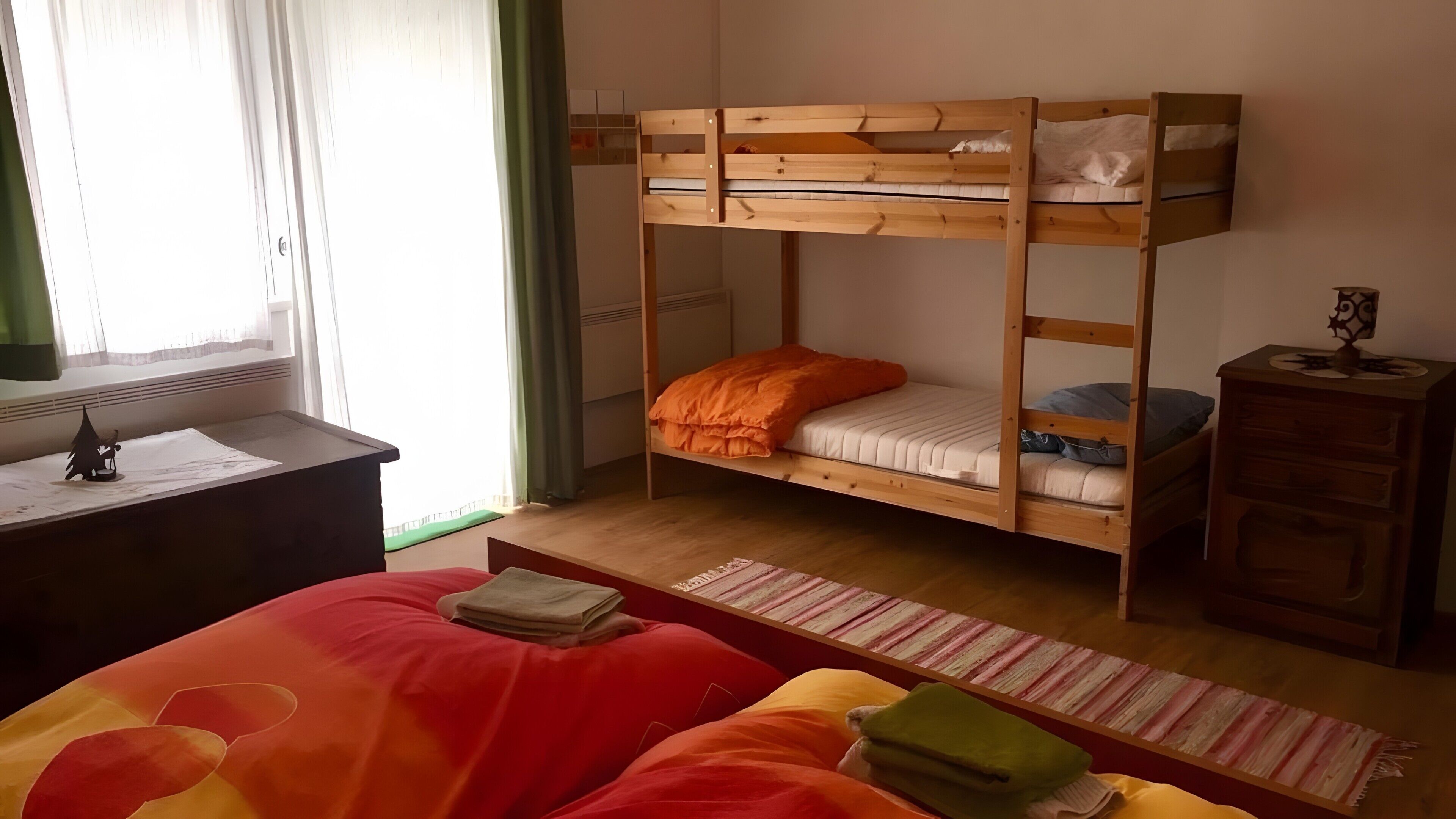A bunk bed with two levels, a desk with a lamp, and a window with curtains.