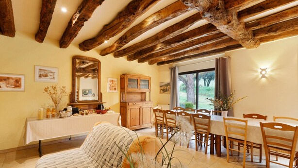 Un área de comedor con una mesa y sillas de madera, un sofá y un mueble con puertas de vidrio.
