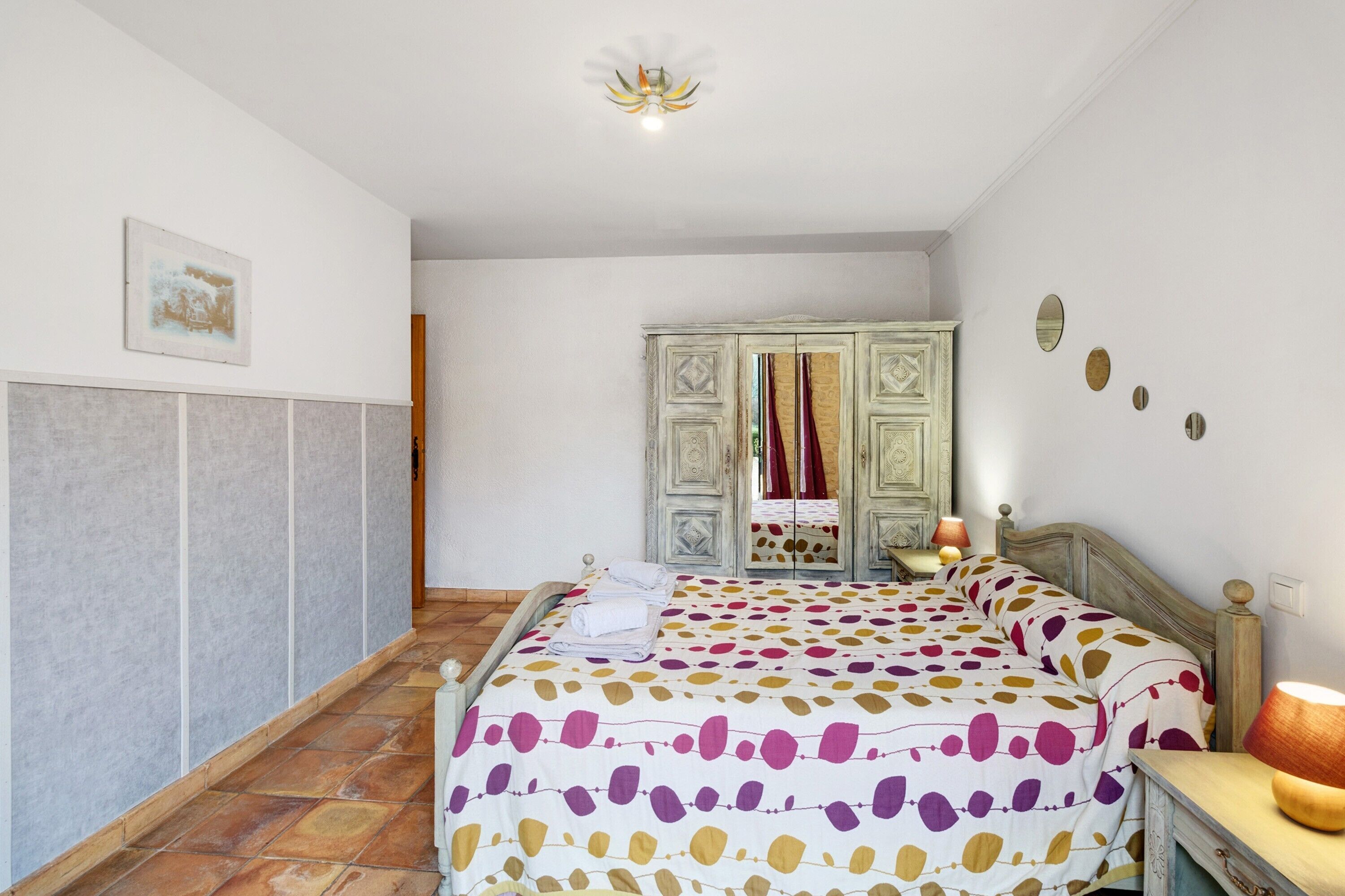 Un dormitorio con cama, armario, espejo y una lámpara en el techo.