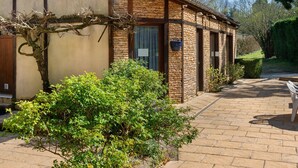 Un edificio de piedra con un patio de ladrillo, un banco y un pequeño jardín.