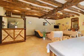 A rustic interior with exposed wooden beams, a stone counter, a sofa, and a dining table.