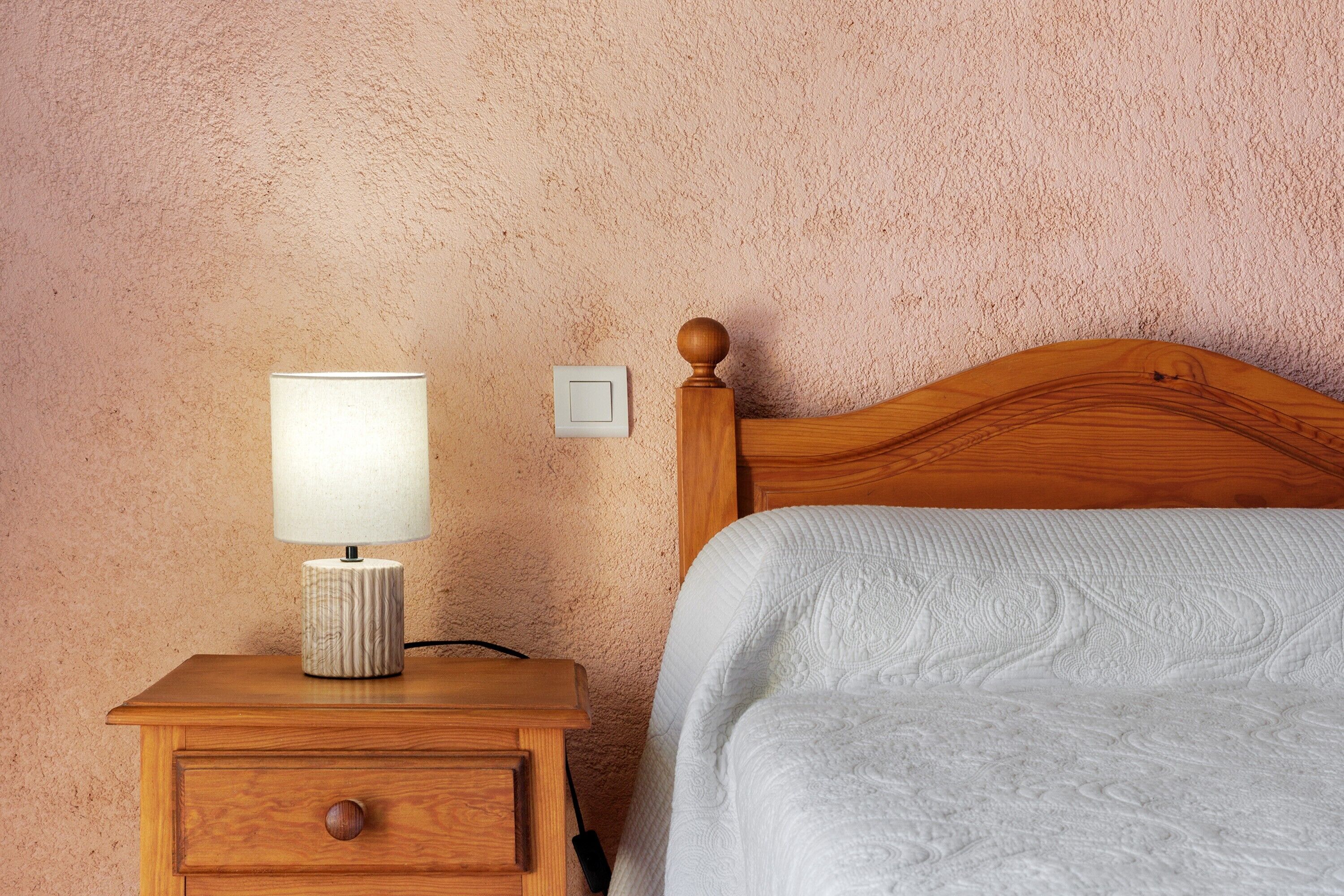 Une table de chevet en bois avec une lampe, un lit avec une tête de lit et un mur à motifs.