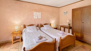 Un dormitorio con dos camas de madera, mesitas de noche con lámparas, un armario y un cuadro colgado en la pared.