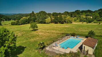A rectangular swimming pool with a wooden deck and lounge chairs, surrounded by a grassy area with trees.