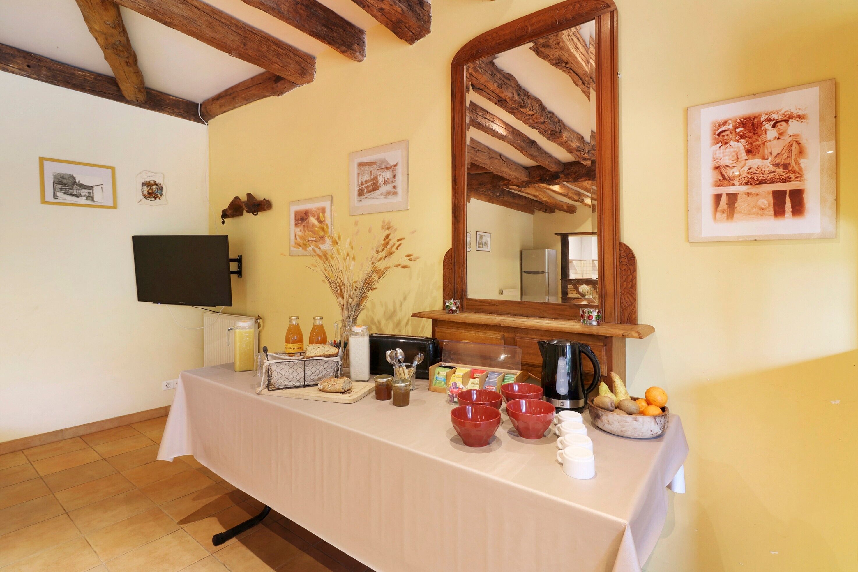 A room with a table set for breakfast, a television, and framed pictures on the wall.