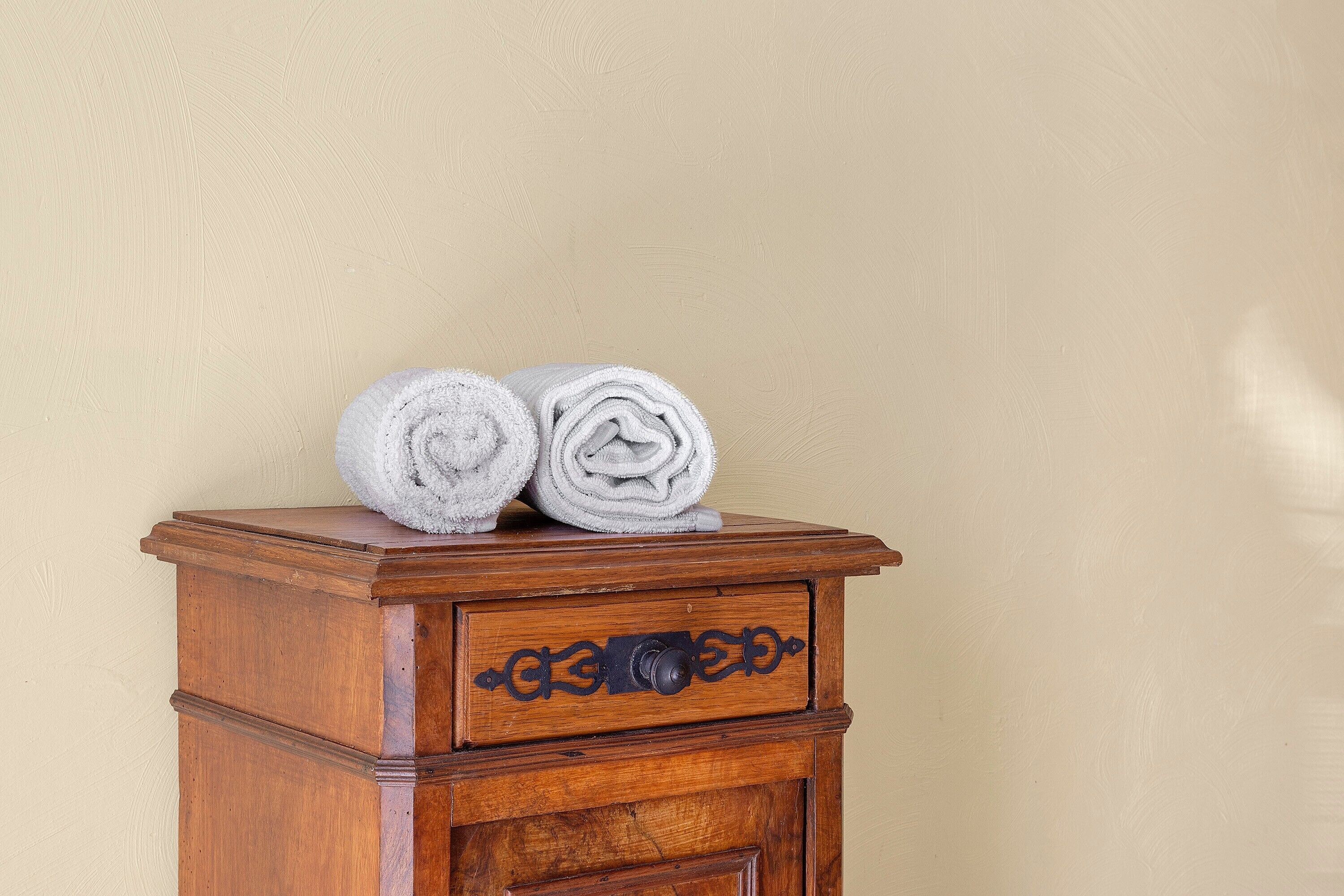A wooden dresser with two rolled towels on top and a drawer below.
