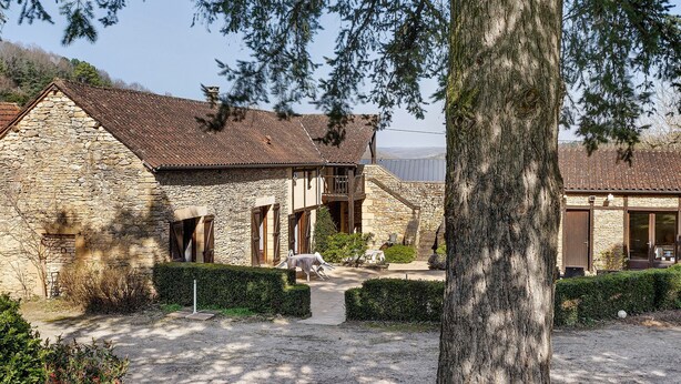 Un bâtiment en pierre doté d’un toit en pente, d’un balcon en bois et d’une allée de gravier menant à une statue de cheval blanc.