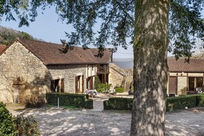 A stone building with a sloped roof, a wooden balcony, and a gravel driveway leading to a white horse statue. - Guest Room “Sarlat B&B with Heated Pool, Large Garden and Wi-Fi” (Sarlat-la-Canéda)