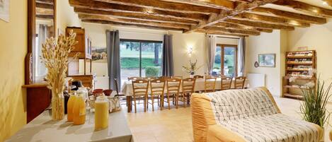 A living room with a sofa, dining table, chairs, wooden beams, and a bookshelf.