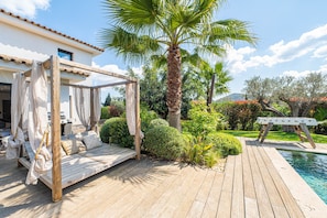 Une terrasse en bois avec un lit à baldaquin, une piscine et une végétation luxuriante.