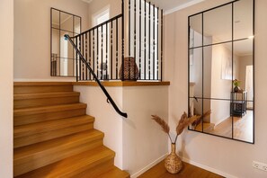 A wooden staircase with a black railing, a large mirror, and a vase with dried plants.