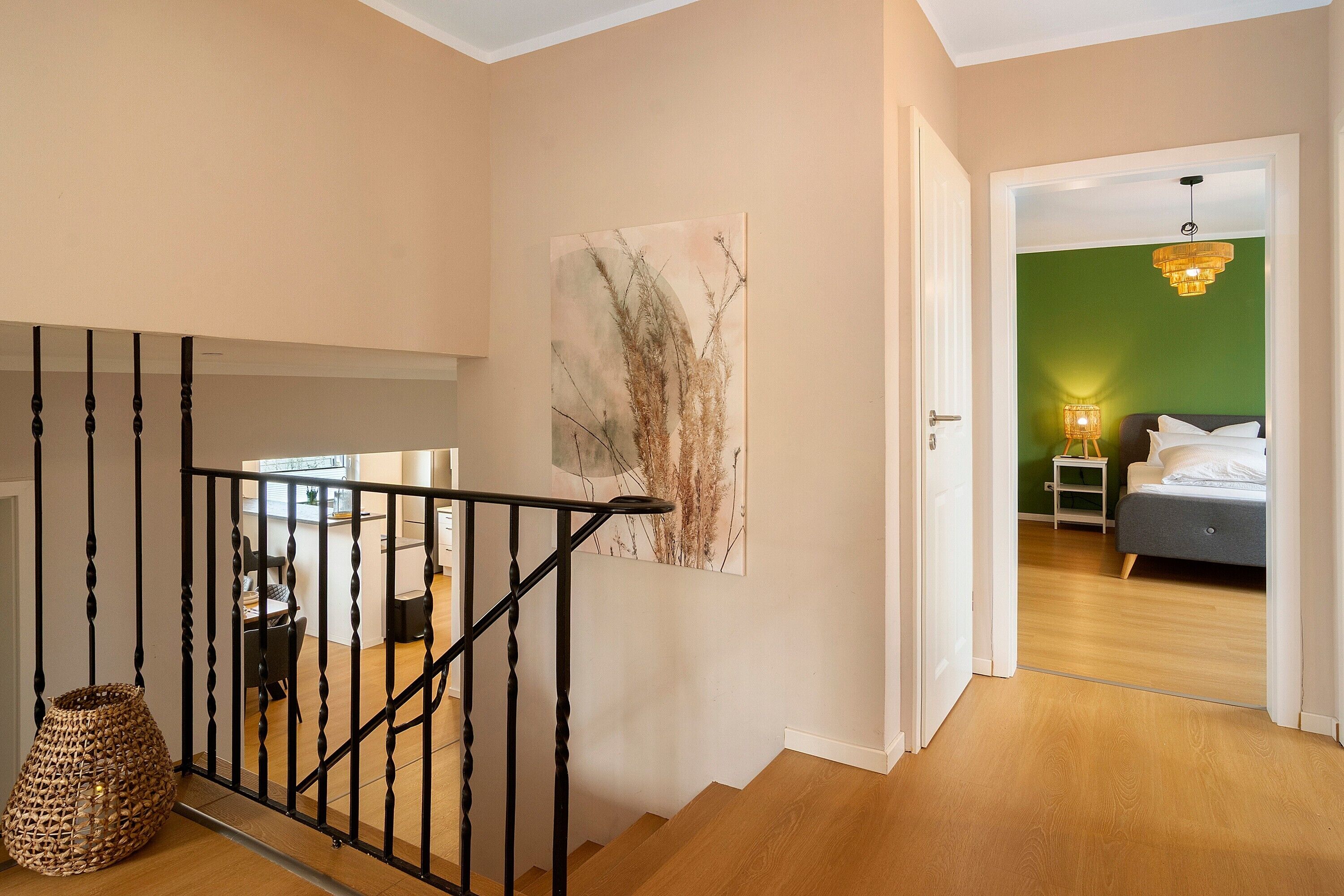 A staircase leading to a bedroom with a green wall, a bed, and a hanging light fixture.