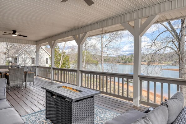 A covered outdoor deck with a fire feature, seating, and a view of a lake.