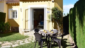 A yellow building with a patio area featuring a round table and chairs, a small garden, and a clear sky. - Ad1000 in Oliva With 2 Bedrooms and 1 Bathrooms (Oliva)