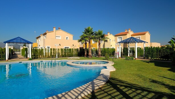 A swimming pool with a surrounding lawn, palm trees, and a building with a yellow facade. - Ad1000 in Oliva With 2 Bedrooms and 1 Bathrooms (Oliva)