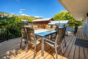 An outdoor deck with a table and chairs, a barbecue grill, and a view of a hilly landscape.