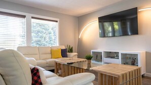 Een moderne woonkamer met een witte bank, een glazen salontafel en een flatscreen televisie die aan de muur is bevestigd.
