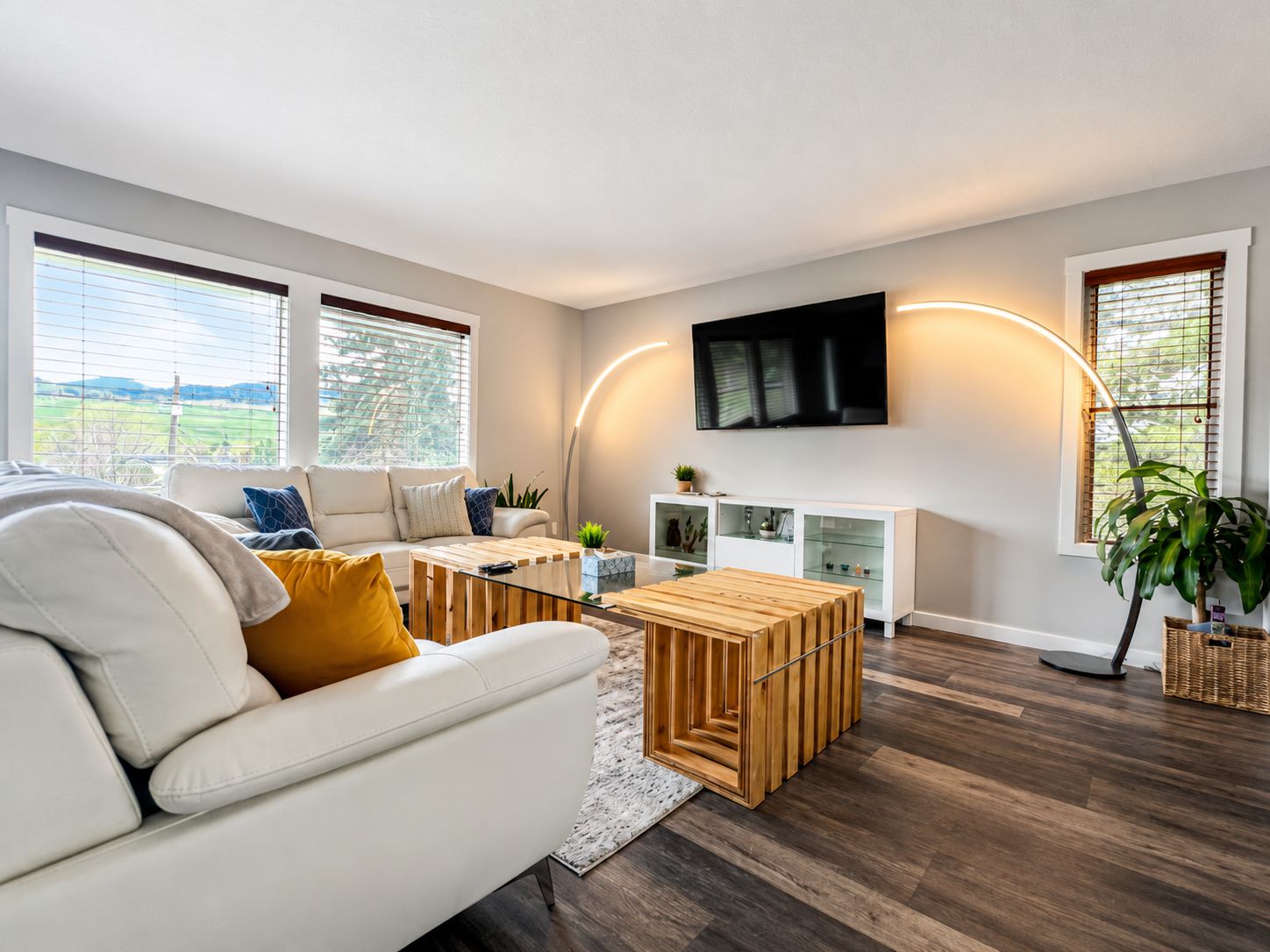 A modern living room with a white sofa, wooden coffee table, and a flat-screen TV mounted on the wall.