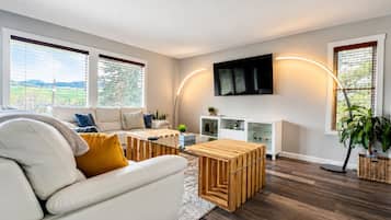 A modern living room with a white sofa, wooden coffee table, and a flat-screen TV mounted on the wall.