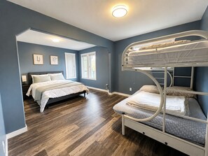 A bedroom with a bunk bed, a single bed, wooden flooring, and a ceiling light.