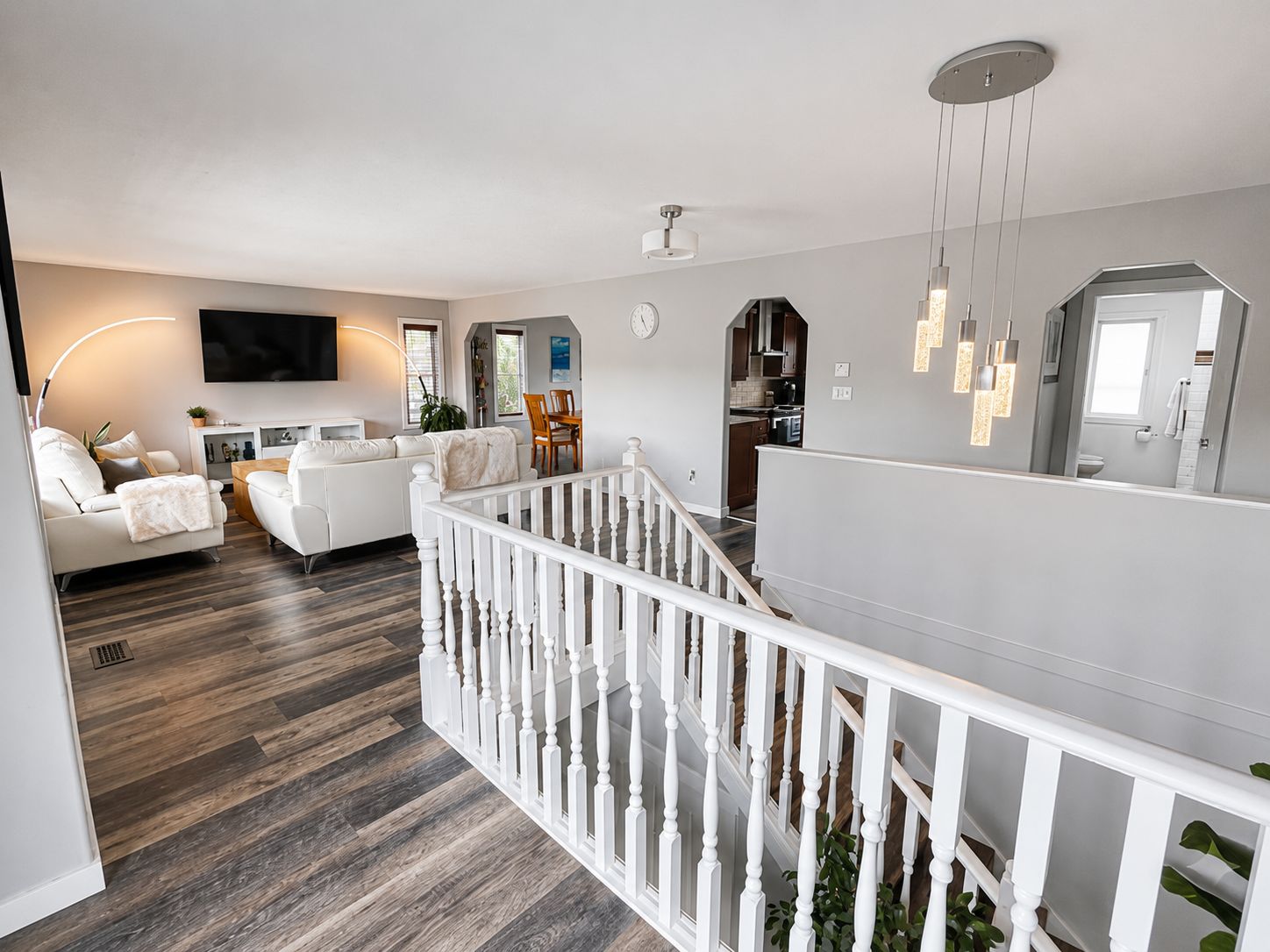 A modern living room with a white sofa, a dining table, and a staircase with a white railing.
