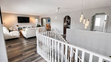 A modern living room with a white sofa, a dining table, and a staircase with a white railing.