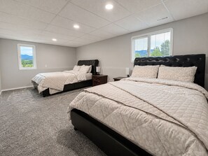 A bedroom with two beds, a carpeted floor, and a window with a view of trees. - Spacious Vernon Retreat w/ Game Room, BBQ Patio & Turf Yard (Vernon)