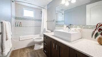 A modern bathroom with a bathtub, toilet, and vanity with a large mirror.