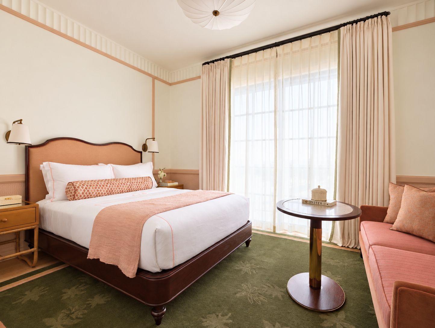 A hotel room with a bed, bedside tables, a round table, a sofa, and a large window with curtains.