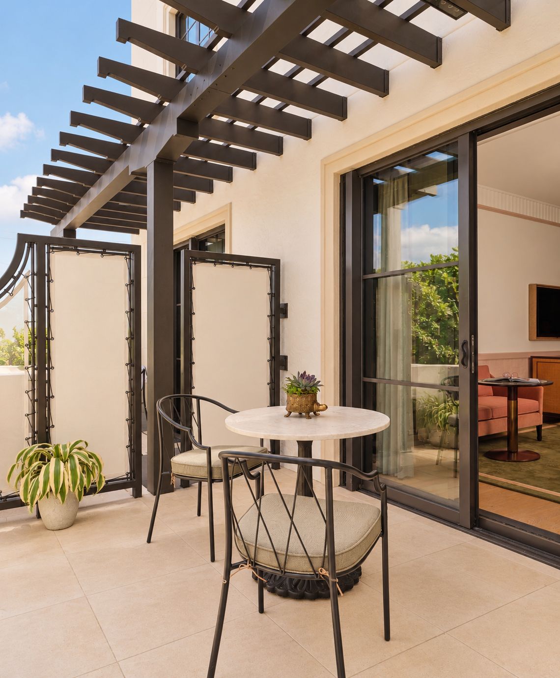 A modern outdoor patio with a round table and chairs, a potted plant, and a pergola structure.